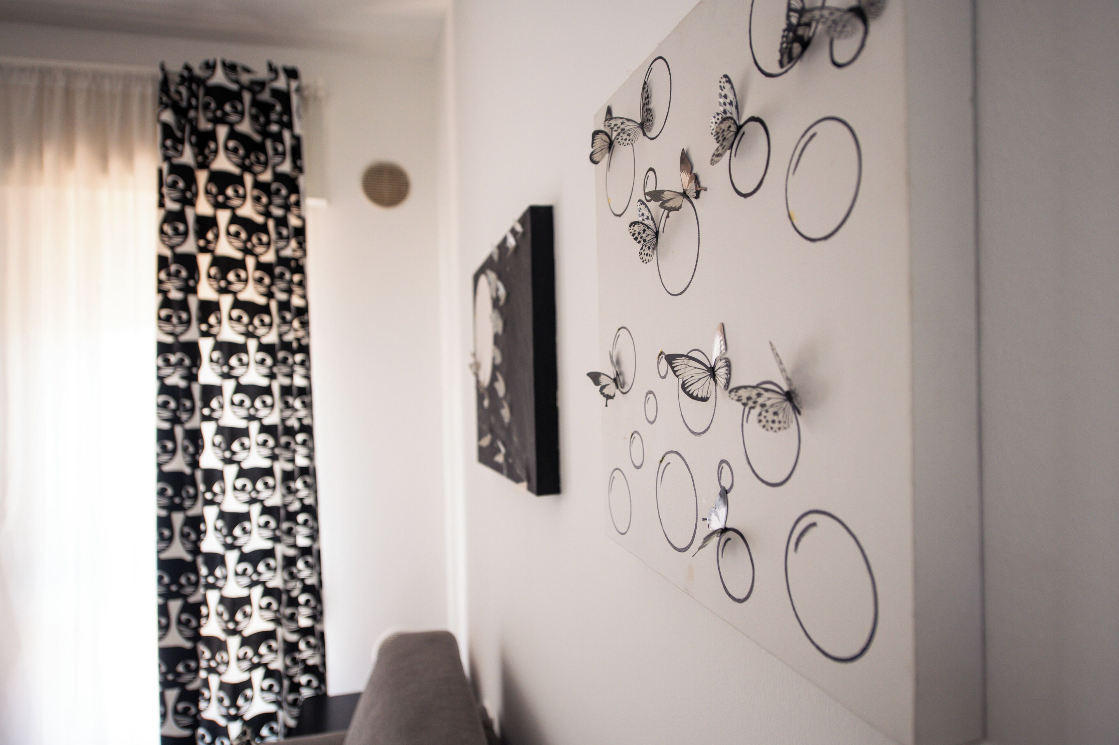 Una habitación con cortina estampada, pared decorada con mariposas y un cuadro enmarcado.