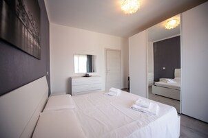 Ein modernes Schlafzimmer mit einem großen Bett, einem Schminktisch, einem Spiegel und einem begehbaren Kleiderschrank.