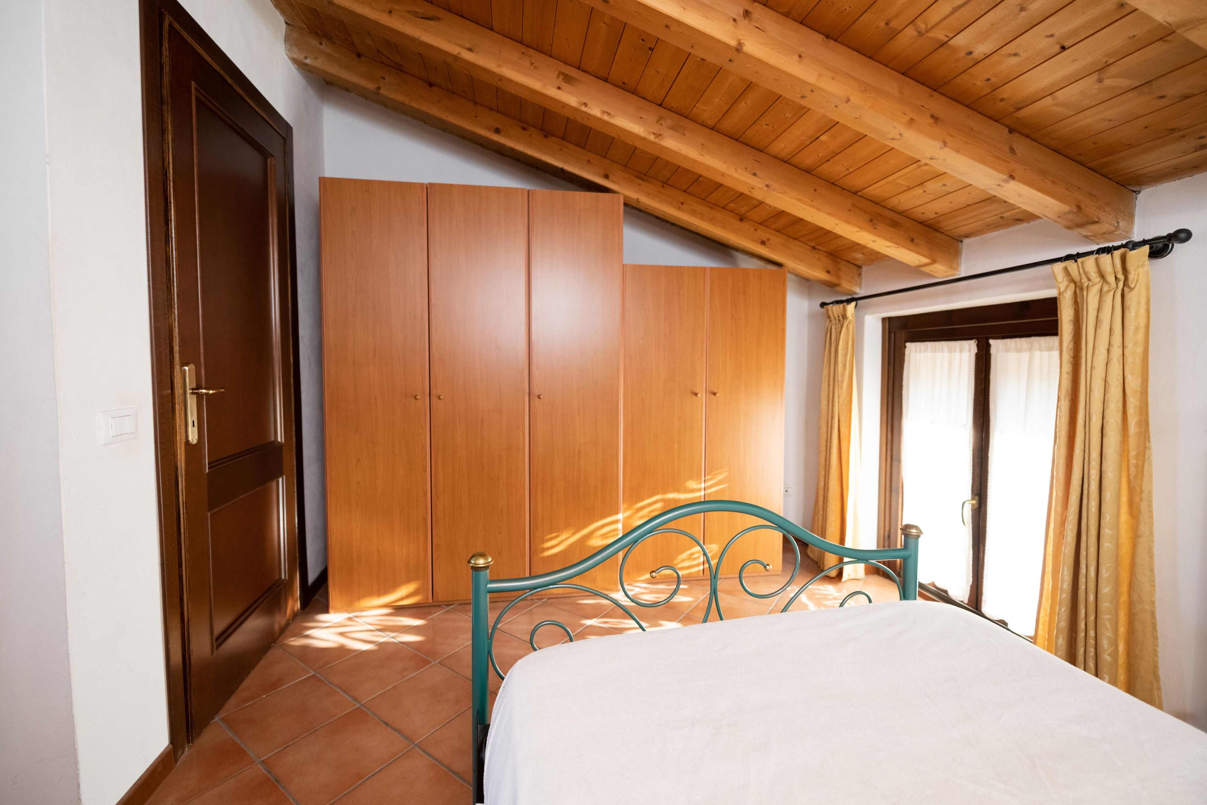 Ein Schlafzimmer mit Bett, Holzschrank und einem fenster mit Vorhängen.