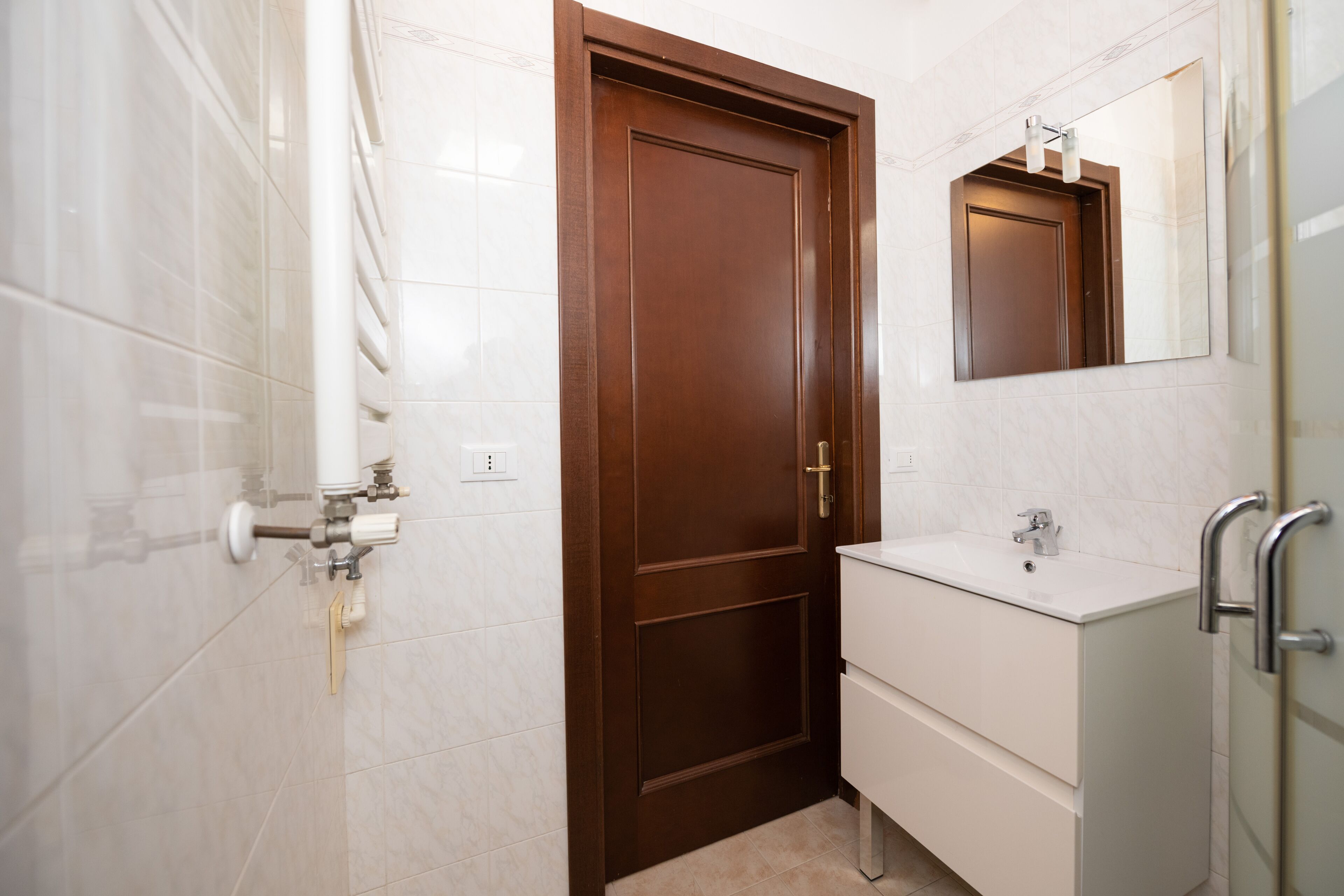 Un bagno con una porta in legno, un lavandino bianco e uno specchio sopra.