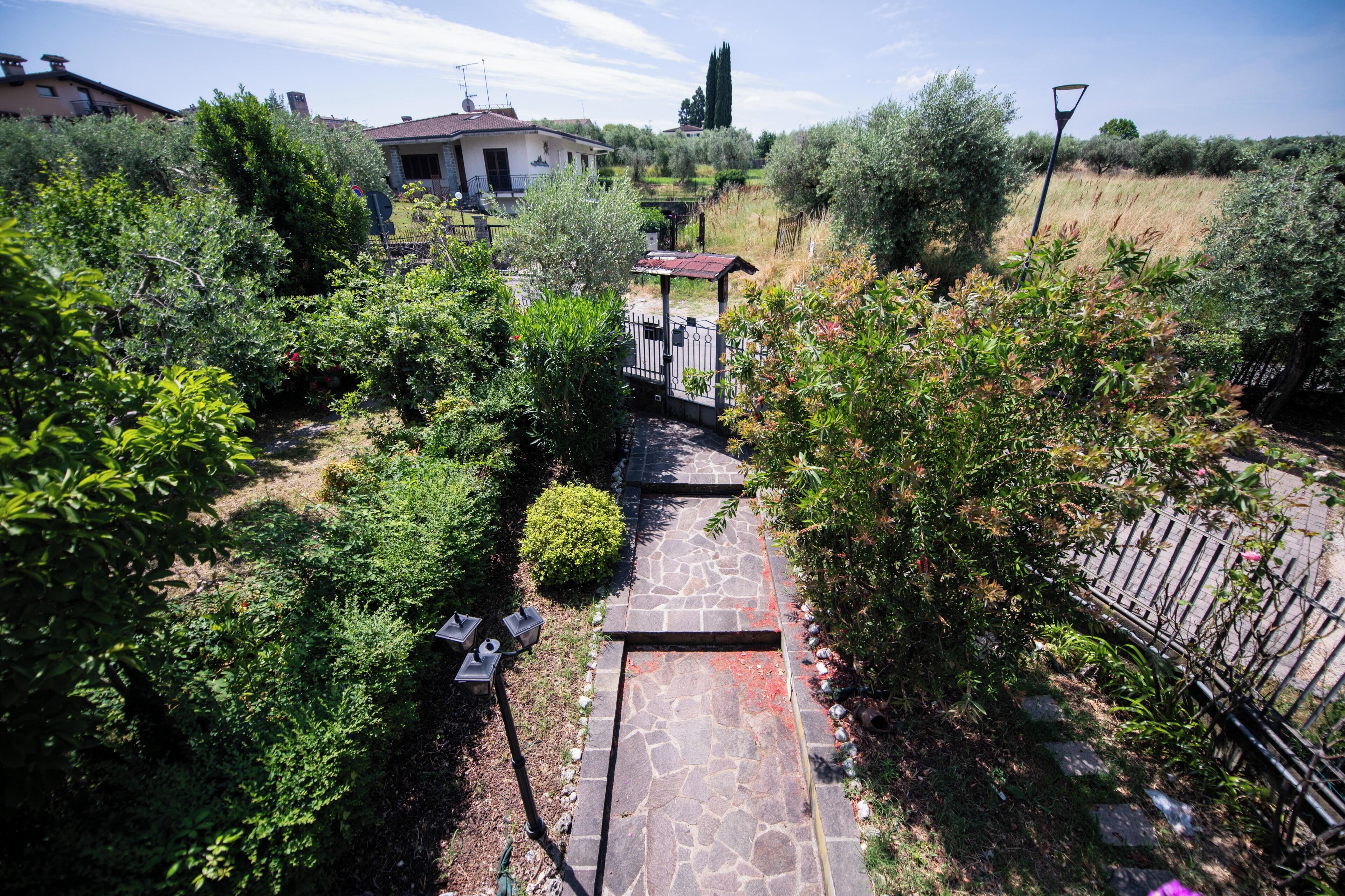 Un vialetto in pietra conduce a un’area relax coperta, immersa nel verde e con una casa sullo sfondo.