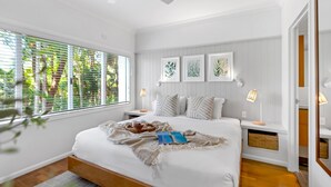 A bedroom with a large bed, a bedside table, a nightstand, and a window with blinds. - Belle Escapes 42 Alamanda Palm Cove (Palm Cove)