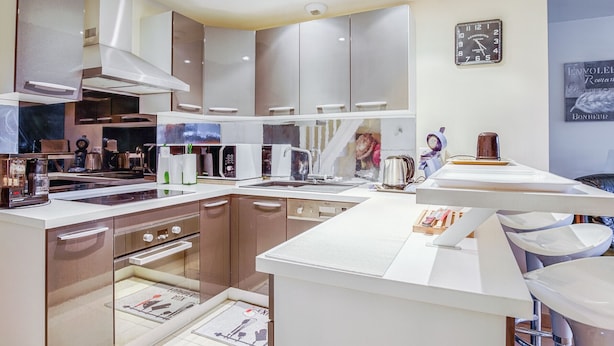 Eine moderne Küche mit Edelstahlgeräten, einem Einbauofen und einer Mikrowelle.  Auf der Arbeitsfläche befindet sich ein Spülbecken mit Wasserhahn, eine Kaffeemaschine und ein Wasserkocher. Das Fenster ist groß und an der Wand hängt eine Uhr.