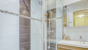 Ein modernes Badezimmer mit einer gläsernen Duschkabine, weißen und grauen Fliesen, einem Holzbadezimmermöbel und einem Spiegel über dem Waschbecken.