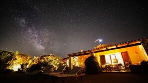 Nachtszene mit Sternenhimmel, einem Gebäude mit Satellitenschüssel und Liegestühlen.