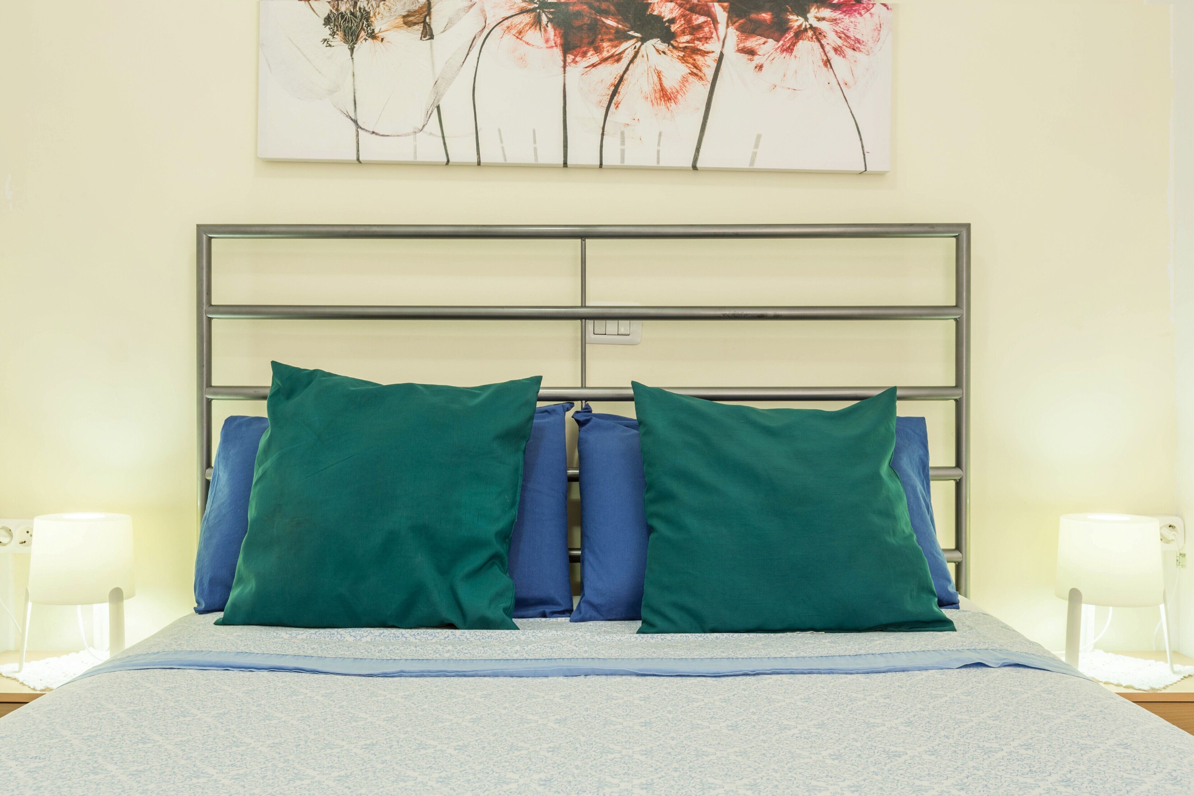 A bed with a metal frame, green and blue pillows, and a white bedspread.