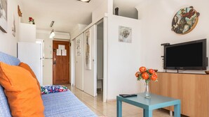 Un salon avec un canapé, un téléviseur et une petite table sur laquelle est posé un vase de fleurs.