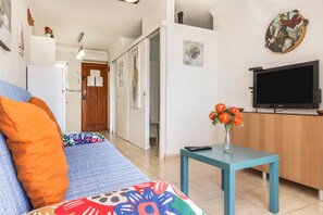 Uma sala de estar com sofá, televisão e uma mesa pequena com um vaso de flores.