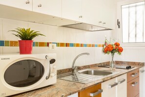 Una cocina con microondas, fregadero, armarios y una planta en maceta.