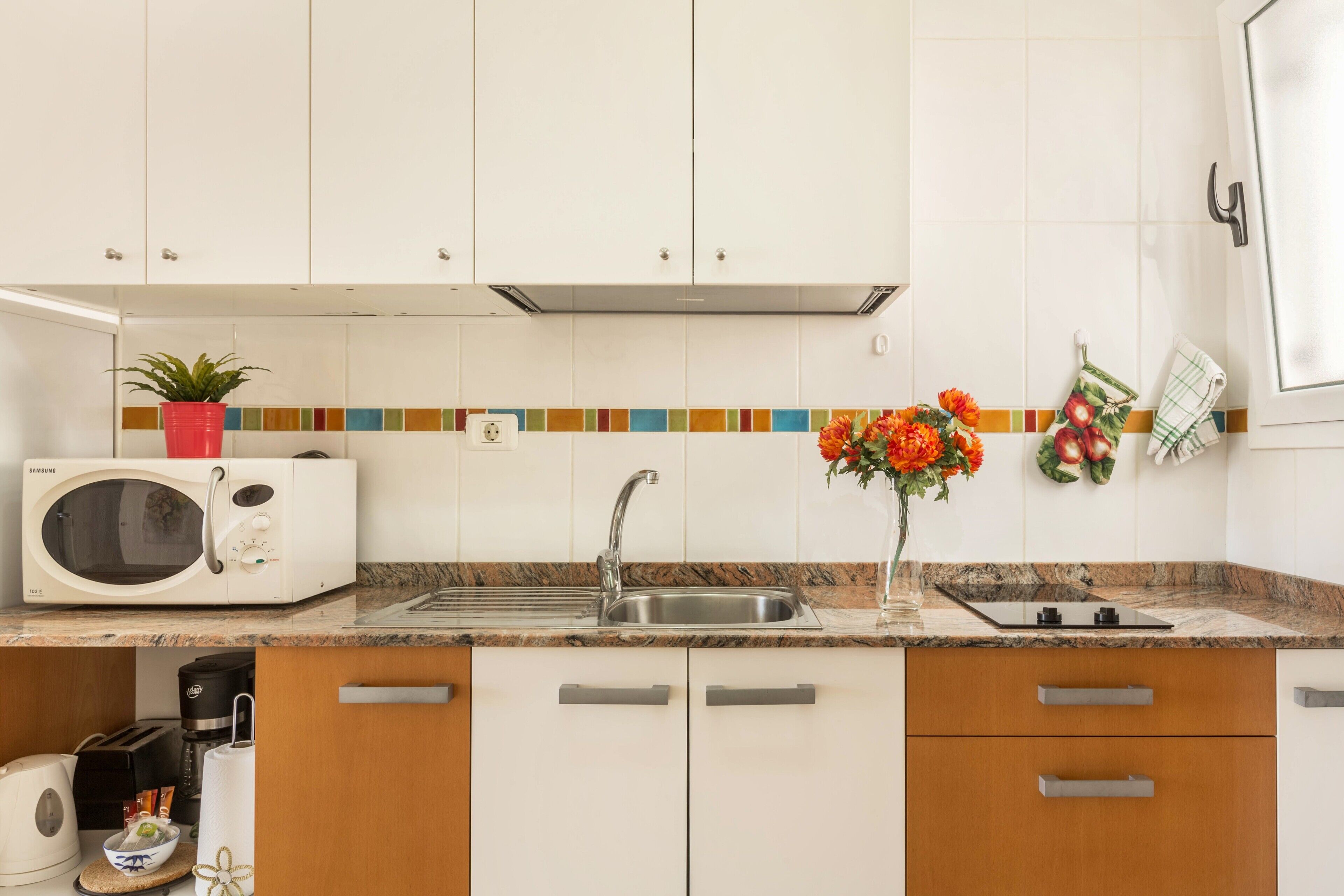 Een keuken met witte kastjes, een magnetron, een spoelbak en een aanrecht met een streepjes achterwand.