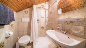 Baño con ducha, inodoro, lavamanos y toallero.