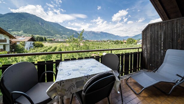 Een balkon met een tafel en stoelen, met uitzicht op een bergachtig landschap.