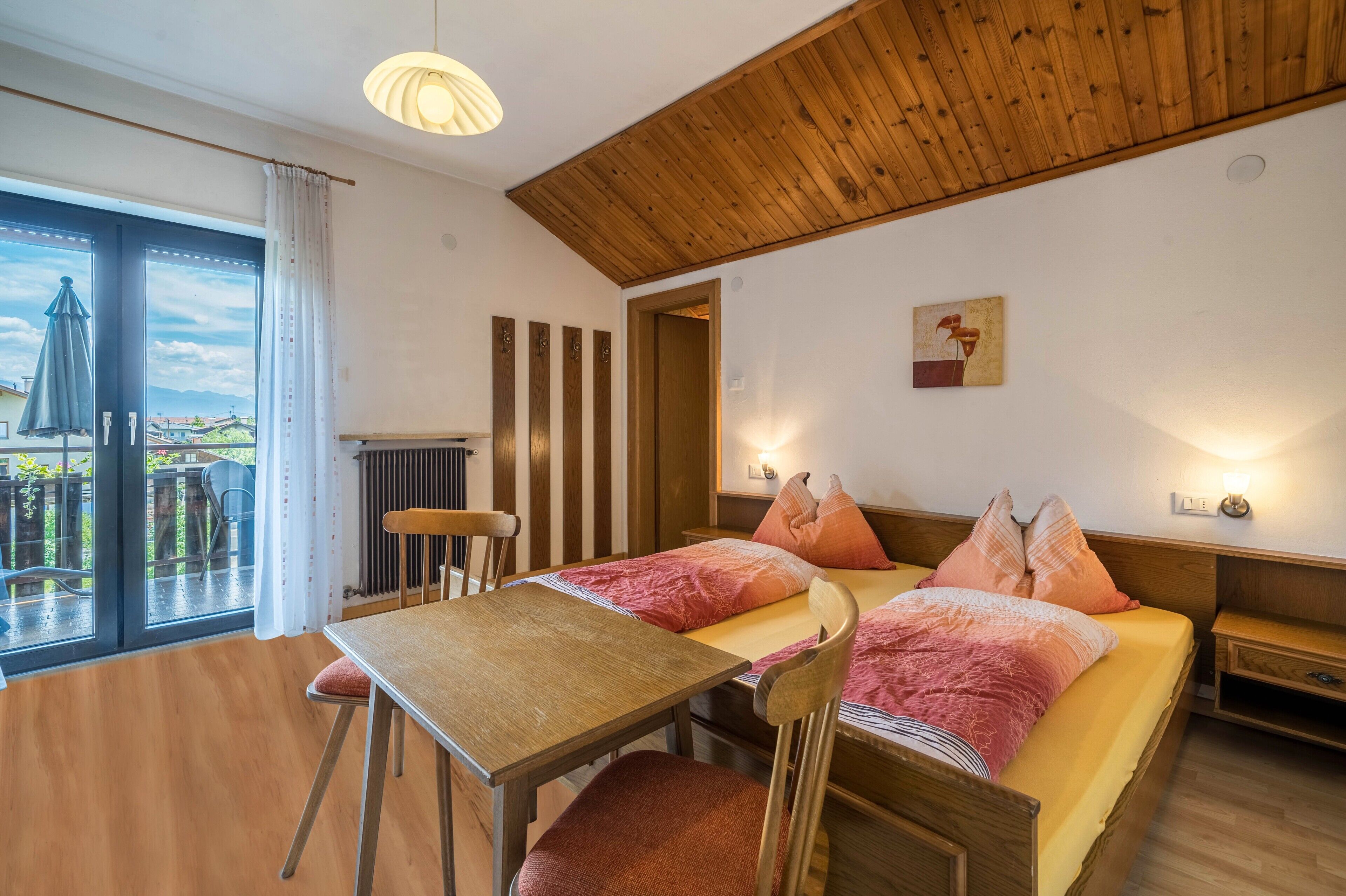Una habitación con dos camas, una mesa, sillas, vistas a través de un ventanal grande y un techo de madera.