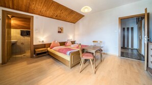 Una camera da letto con soffitto in legno, un letto con lenzuola rosa, un tavolo in legno con una sedia e un piccolo comodino.