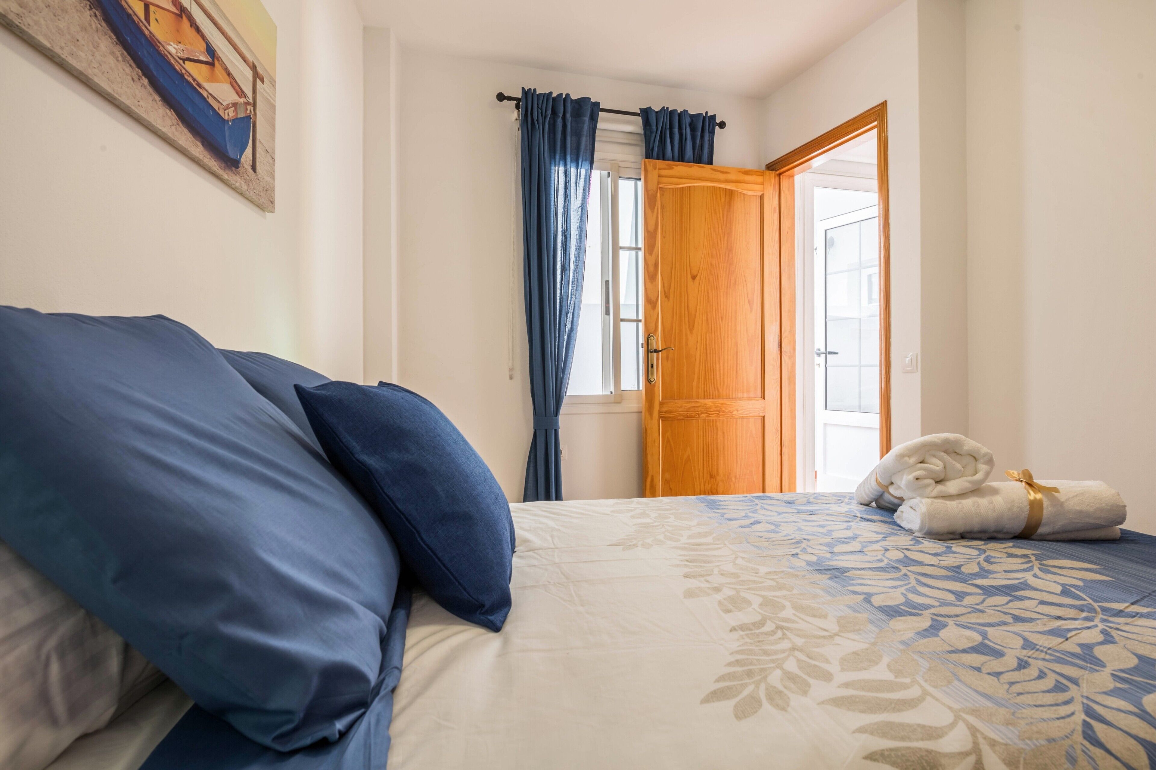 Ein Schlafzimmer mit Bett, Kissen, einem Fenster mit Vorhängen, einer Tür und einem Handtuch auf dem Boden.