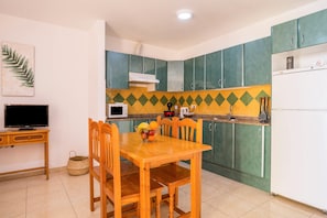A kitchen with green cabinets, a wooden dining table, and a microwave. - Cozy Apartment "Las Playitas" near the Beach with Wi-Fi & Terrace (Tuineje)