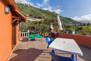 Una terraza con mesa y sillas, vista a una ladera y un edificio con balcón.