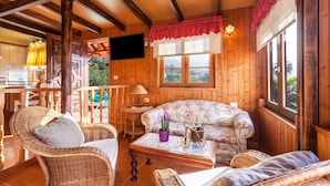 A wooden interior with wicker furniture, a sofa, a television, and a window with a view.