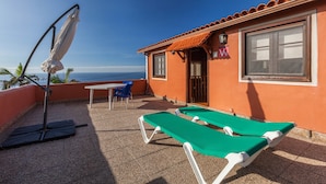 A terrace with two green lounge chairs, a table, and a chair, overlooking the sea.