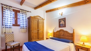 Quarto com cama de madeira, mesa de cabeceira com abajur, guarda-roupa, cadeira e janela com cortinas.