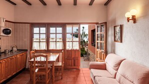 Une cuisine avec des meubles en bois, une table à manger et des chaises, un canapé, et une vue sur un espace extérieur accessible par une porte, où se trouve un banc.