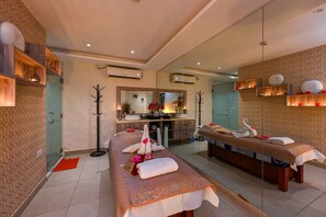 Un cuarto de spa con una camilla de masaje, un espejo y estantes con objetos decorativos.