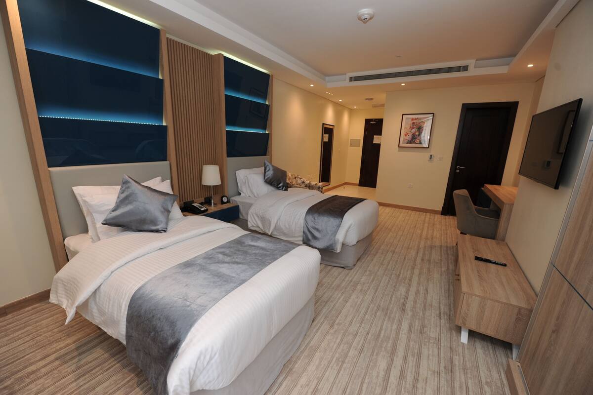 A hotel room with two beds, a desk, a TV, and a large window with a view.