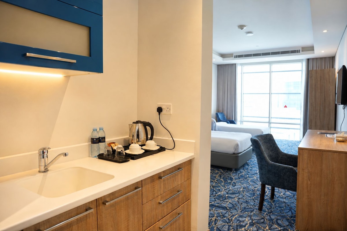 Habitación de hotel con kitchenette, cama, escritorio y silla.