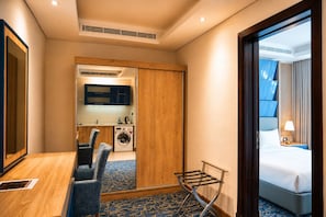 Quarto de hotel com cama, escrivaninha, cadeira, máquina de lavar e espelho.