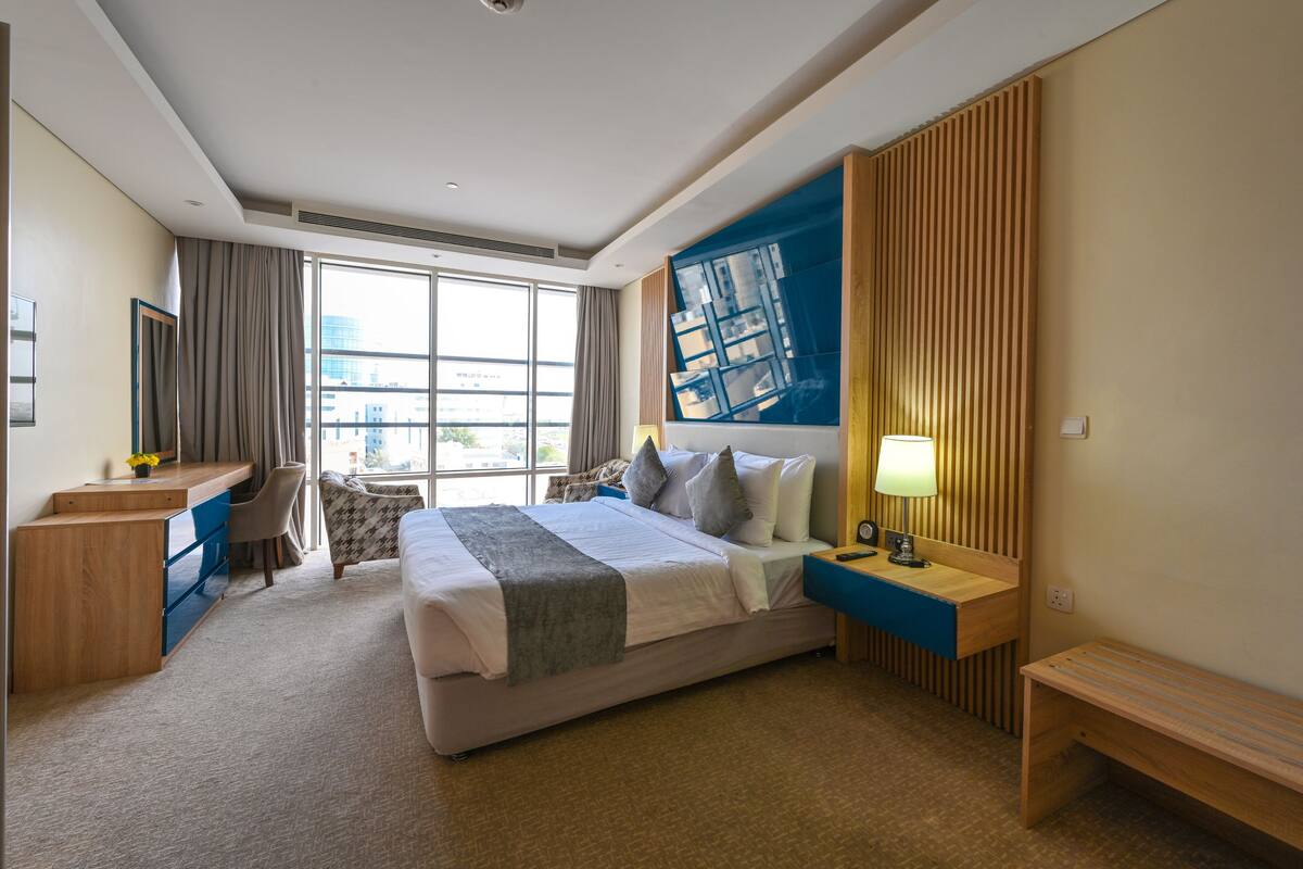 A modern hotel room with a large bed, a desk, a chair, and a view of the city.