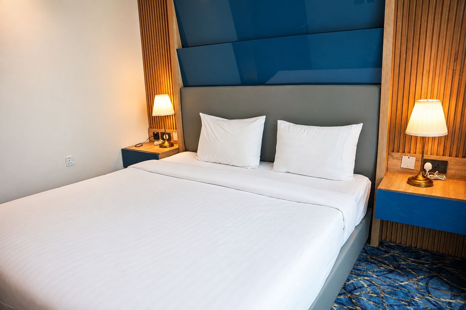 Una habitación de hotel con una cama grande, dos mesitas de noche con lámparas y una alfombra estampada.