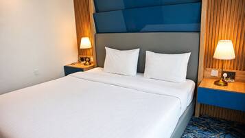 Una habitación de hotel con una cama grande, dos mesitas de noche con lámparas y una alfombra estampada.