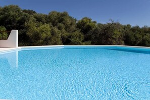 Piscina azul cristalina con borde blanco, rodeada de abundante follaje verde.
