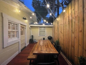 A wooden deck with a table and chairs, string lights, and a wooden fence. - Steps to Dining, Shopping, 3 Minute Walk to Beach (Folly Beach)