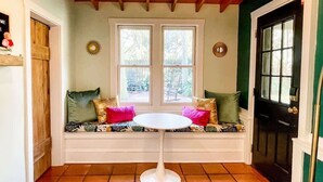 A room with a white bench with cushions, a round table, and two windows. - Steps to Dining, Shopping, 3 Minute Walk to Beach (Folly Beach)