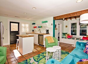 Un espacio habitable compacto con kitchenette, comedor y zona de estar con sofá y sillones.
