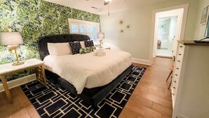 A bedroom with a bed, a nightstand, a ceiling fan, and a door leading to another room. - Steps to Dining, Shopping, 3 Minute Walk to Beach (Folly Beach)