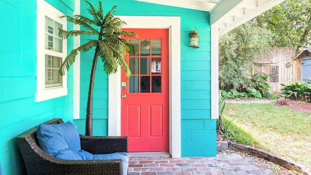 A turquoise house with a red door, a wicker chair, and a palm tree. - Steps to Dining, Shopping, 3 Minute Walk to Beach (Folly Beach)