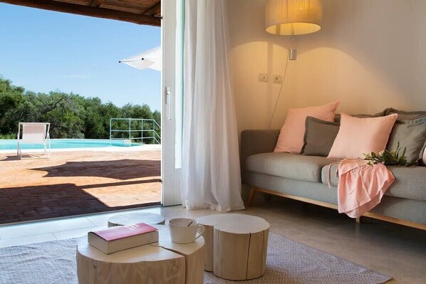 A modern living room with a sofa, pillows, a coffee table, and a view of an outdoor swimming pool.