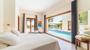 A hotel room with a large bed, a view of a swimming pool, and a door leading to a balcony. - Villa "Son Sard" with Sea & Mountain View, Pool, A/C, Balcony, Garden & Terrace (Son Servera)