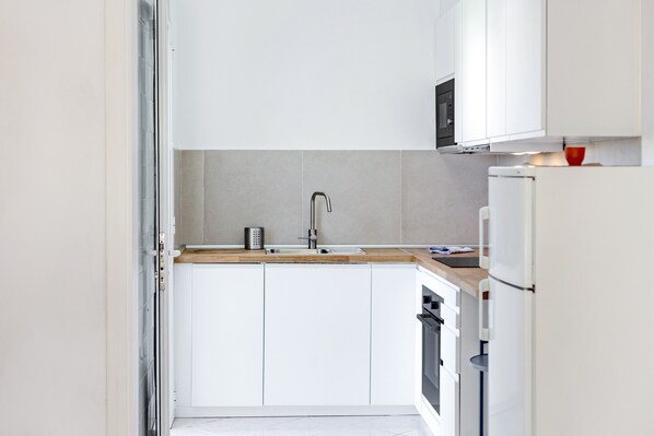 A modern kitchen with white cabinets, a stainless steel sink, a microwave, and a refrigerator.
