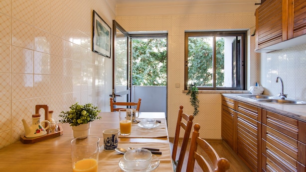 Una cocina con una mesa de comedor para dos, una ventana con vistas a árboles y armarios de madera.