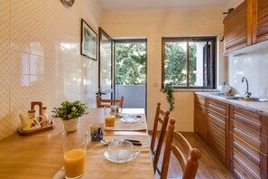 A kitchen with a dining table set for two, a window with a view of trees, and wooden cabinets.