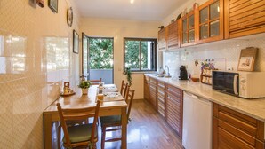 Una cocina con armarios de madera, una mesa de comedor con sillas, un microondas y un ventanal con vistas a árboles.