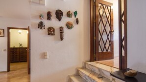Una escalera con escalones de mármol, una puerta de madera con diseño de rombos y una pared con diversas máscaras decorativas.