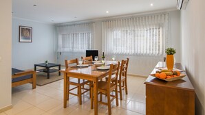 A dining area with a wooden table set for four, a small side table, and a fruit bowl on a wooden cabinet.
