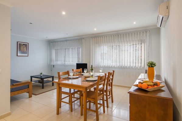 A dining area with a wooden table set for four, a small side table, and a fruit bowl on a wooden cabinet.