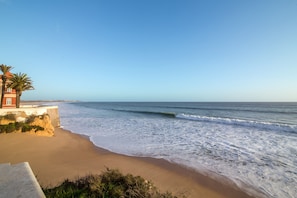 A beach with a building, palm trees, and ocean waves.