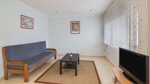 A living room with a sofa, a coffee table, a TV, and two framed artworks on the wall.