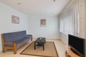 A living room with a sofa, a coffee table, a TV, and two framed artworks on the wall.
